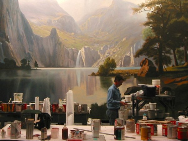 A scenic painter prepares his paint and tools in front of an epic landscape backdrop showcasing the Scenic Paint Department Roles